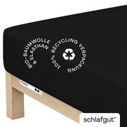 Schwarzes Spannbettlaken aus Bio-Baumwolle und Elasthan auf einer Matratze, mit Hinweis auf 100% recycelte Verpackung, seitliche Perspektive.