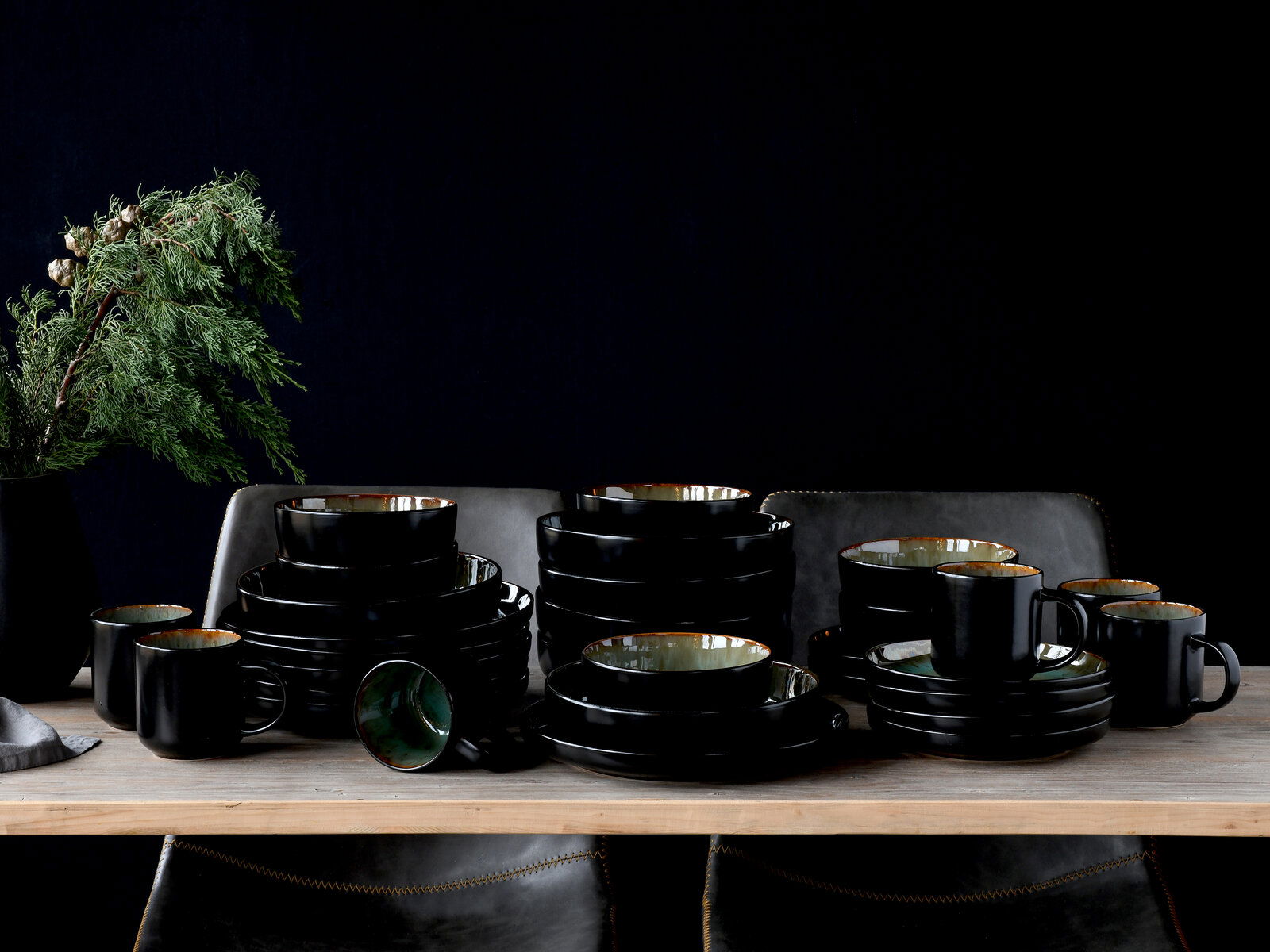 Elegantes 30-teiliges Kombiservice in Schwarz mit grüner Innenseite, auf einem Tisch arrangiert, seitliche Perspektive.