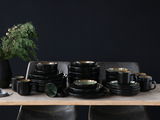Elegantes 30-teiliges Kombiservice in Schwarz mit grüner Innenseite, auf einem Tisch arrangiert, seitliche Perspektive.
