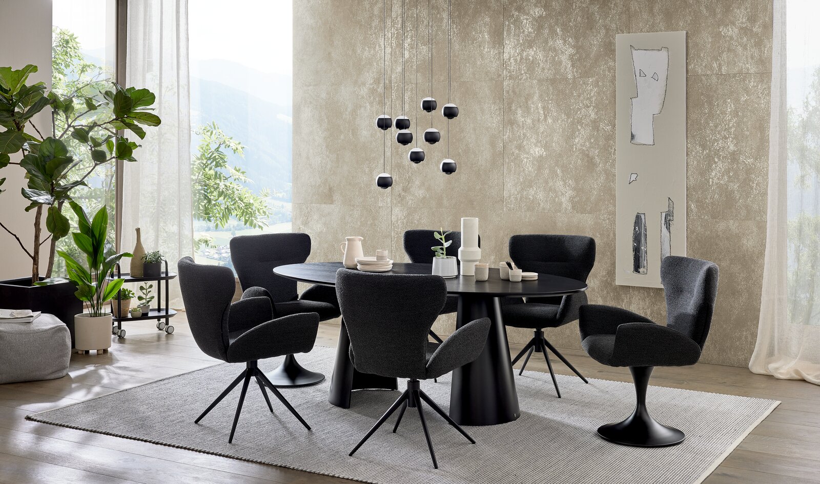 Musterring Armlehnstuhl MR JUSTB! Moderner Essbereich mit einem runden, schwarzen Esstisch und mehreren schwarzen Armlehnstühlen auf einem hellen Teppich. Die Perspektive zeigt den Raum von der Seite mit Blick auf die Tischgruppe und die umgebende Dekoration.