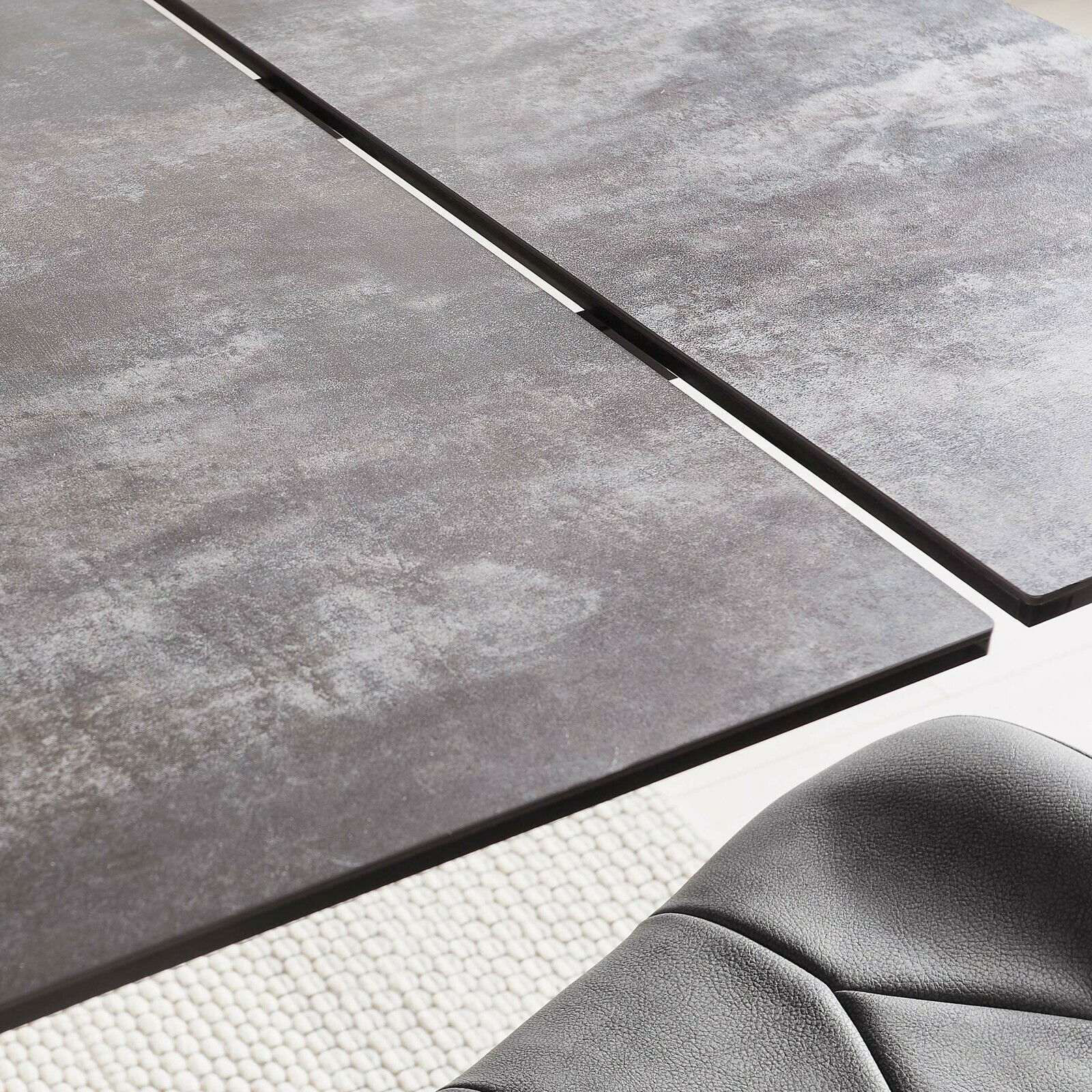 Nahaufnahme eines modernen Esstisches mit grauer, strukturierter Oberfläche und einer eleganten Kante, aus der Vogelperspektive.