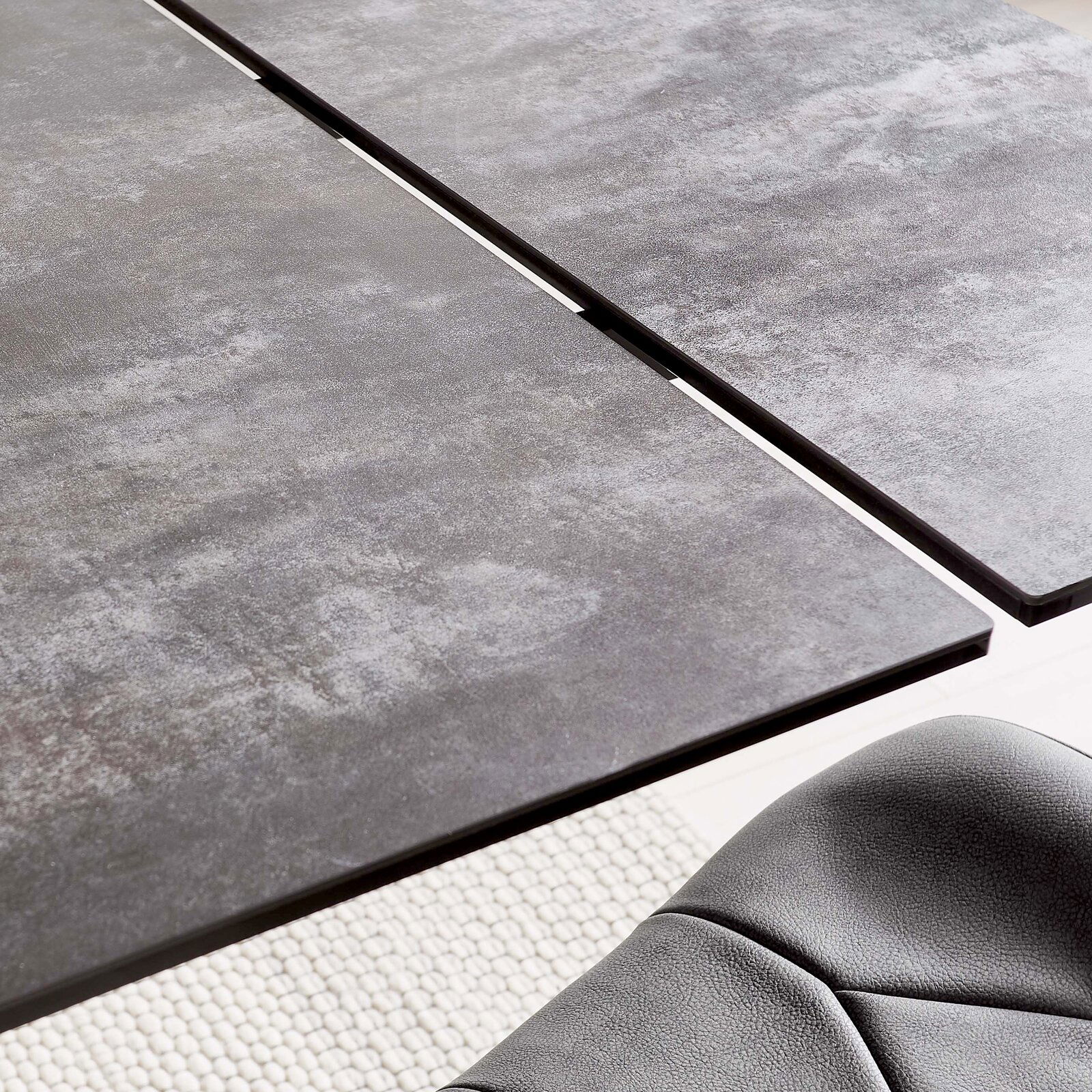 Nahaufnahme eines modernen Esstisches mit grauer, strukturierter Oberfläche und einer eleganten Kante, aus der Vogelperspektive.