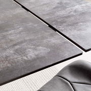 Nahaufnahme eines modernen Esstisches mit grauer, strukturierter Oberfläche und einer eleganten Kante, aus der Vogelperspektive.