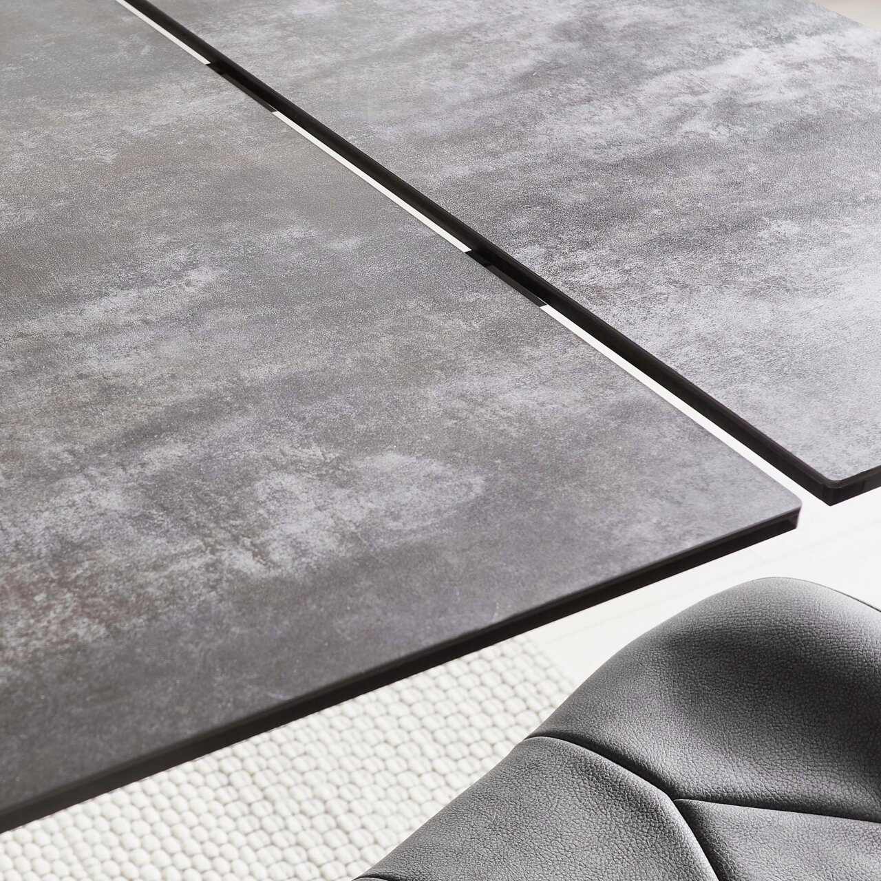 Nahaufnahme eines modernen Esstisches mit grauer, strukturierter Oberfläche und einer eleganten Kante, aus der Vogelperspektive.