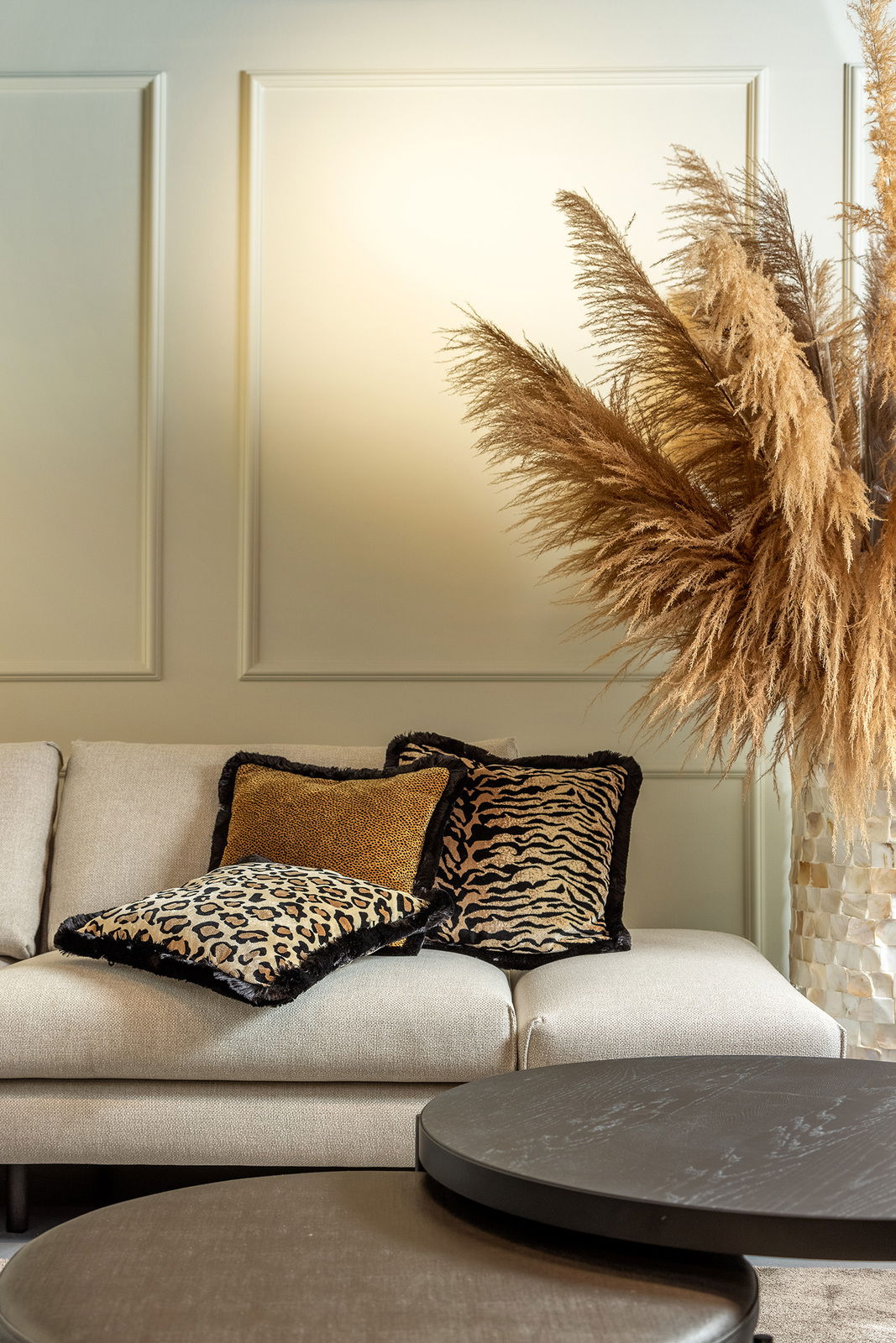 Dekokissen mit Tiermuster auf einem beigen Sofa, umgeben von Pampasgras, aus seitlicher Perspektive fotografiert.