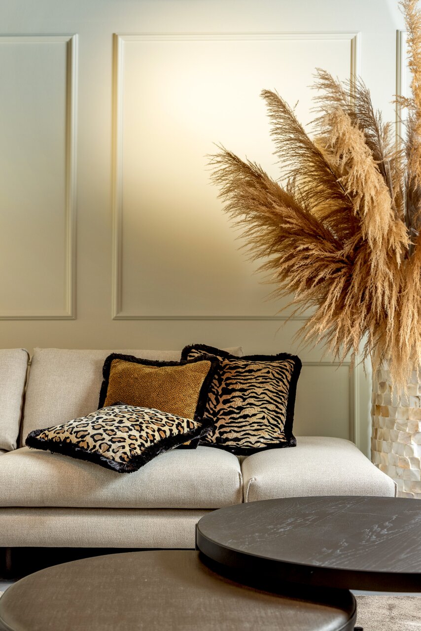 Dekokissen mit Tiermuster auf einem beigen Sofa, umgeben von Pampasgras, aus seitlicher Perspektive fotografiert.