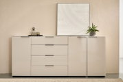 Modernes, weißes Sideboard mit drei Schubladen und zwei Türen, schwarze Griffleisten, dekoriert mit Glasflasche, Tablett, Pflanze und gerahmtem Reliefbild; frontale Ansicht auf Augenhöhe.
