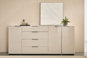 Modernes, weißes Sideboard mit drei Schubladen und zwei Türen, schwarze Griffleisten, dekoriert mit Glasflasche, Tablett, Pflanze und gerahmtem Reliefbild; frontale Ansicht auf Augenhöhe.