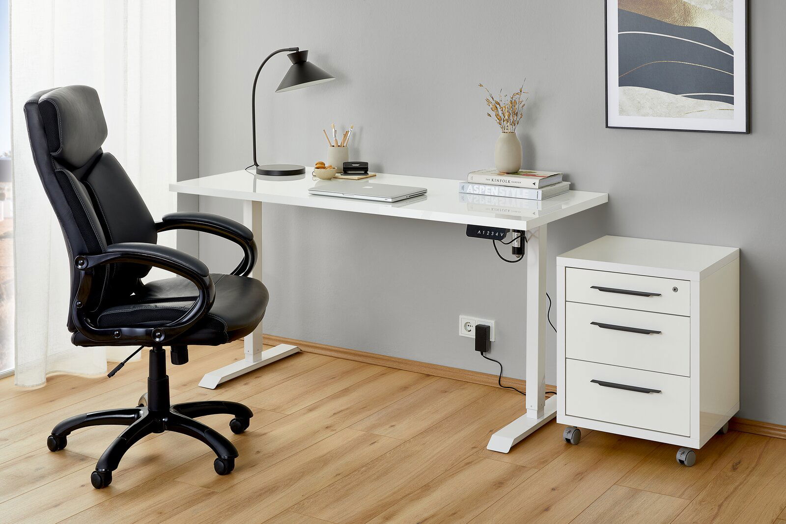 Moderner Arbeitsplatz mit weißer E-Tischplatte, schwarzem Bürostuhl und Rollcontainer, seitliche Perspektive.