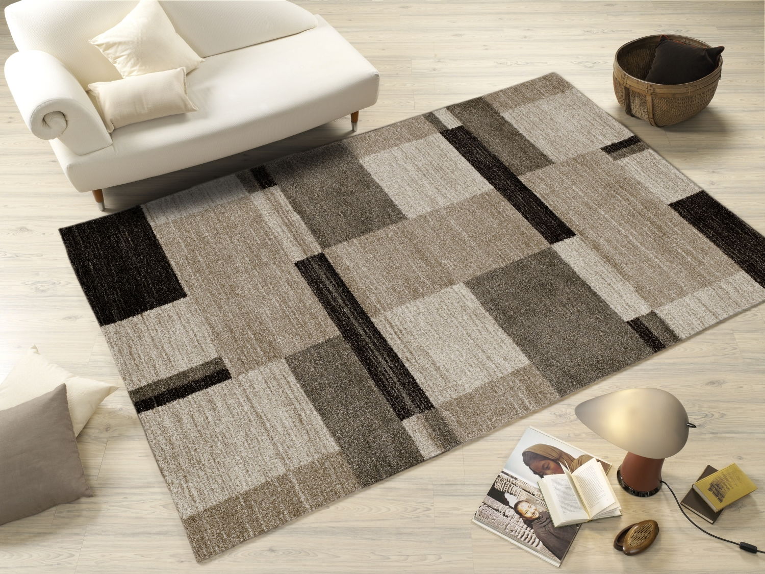 Moderner Teppich in Beige- und Brauntönen mit geometrischem Muster, auf hellem Holzboden neben einem weißen Sofa und Dekorationsgegenständen, aus der Vogelperspektive betrachtet.