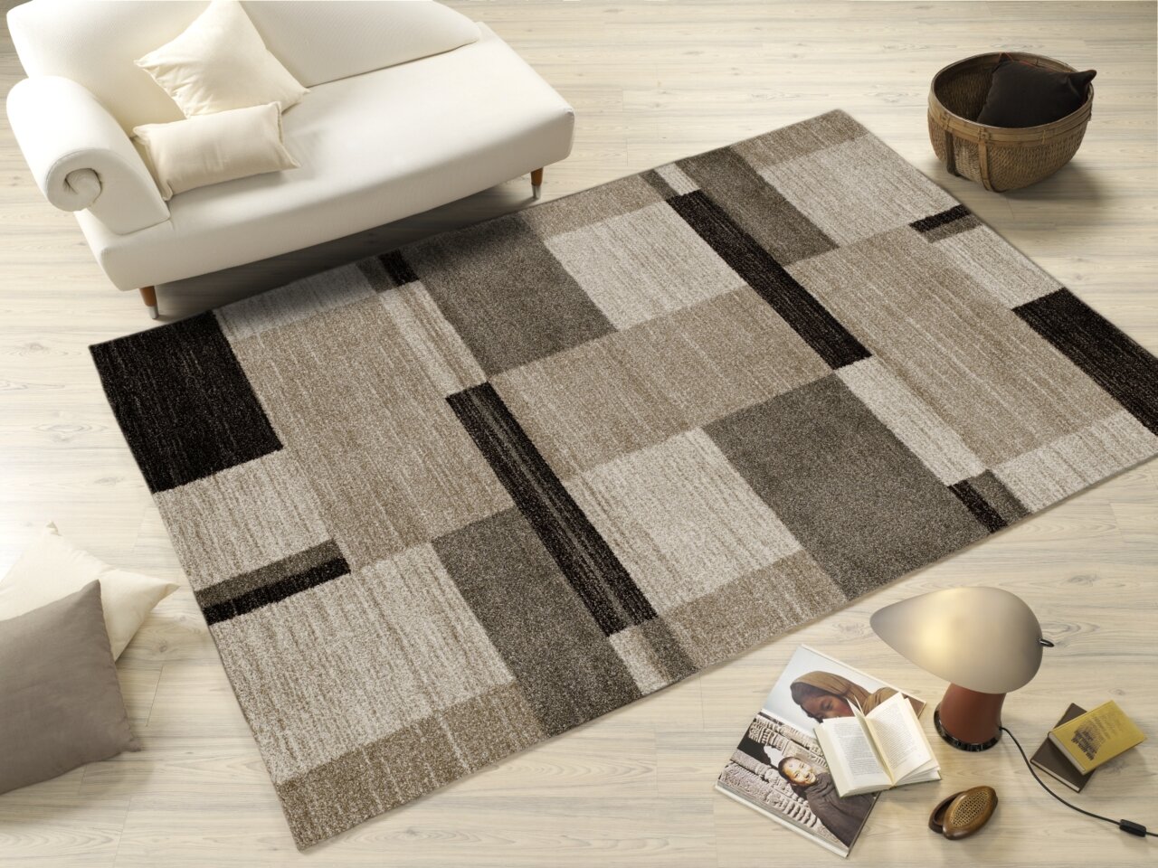 Moderner Teppich in Beige- und Brauntönen mit geometrischem Muster, auf hellem Holzboden neben einem weißen Sofa und Dekorationsgegenständen, aus der Vogelperspektive betrachtet.