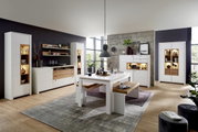 Moderne Wohnzimmermöbel in heller Holzoptik mit Vitrinen, Sideboard, Esstisch und Bank, seitliche Perspektive