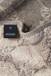 Nahaufnahme eines beigen Gästetuchs mit grauem Muster und einem schwarzen Etikett mit der Aufschrift 'JOOP!'