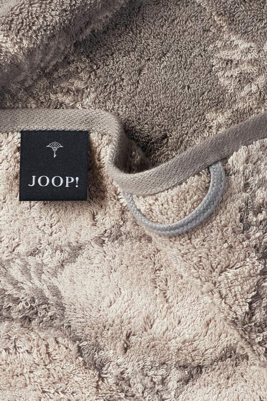 Nahaufnahme eines beigen Gästetuchs mit grauem Muster und einem schwarzen Etikett mit der Aufschrift 'JOOP!'