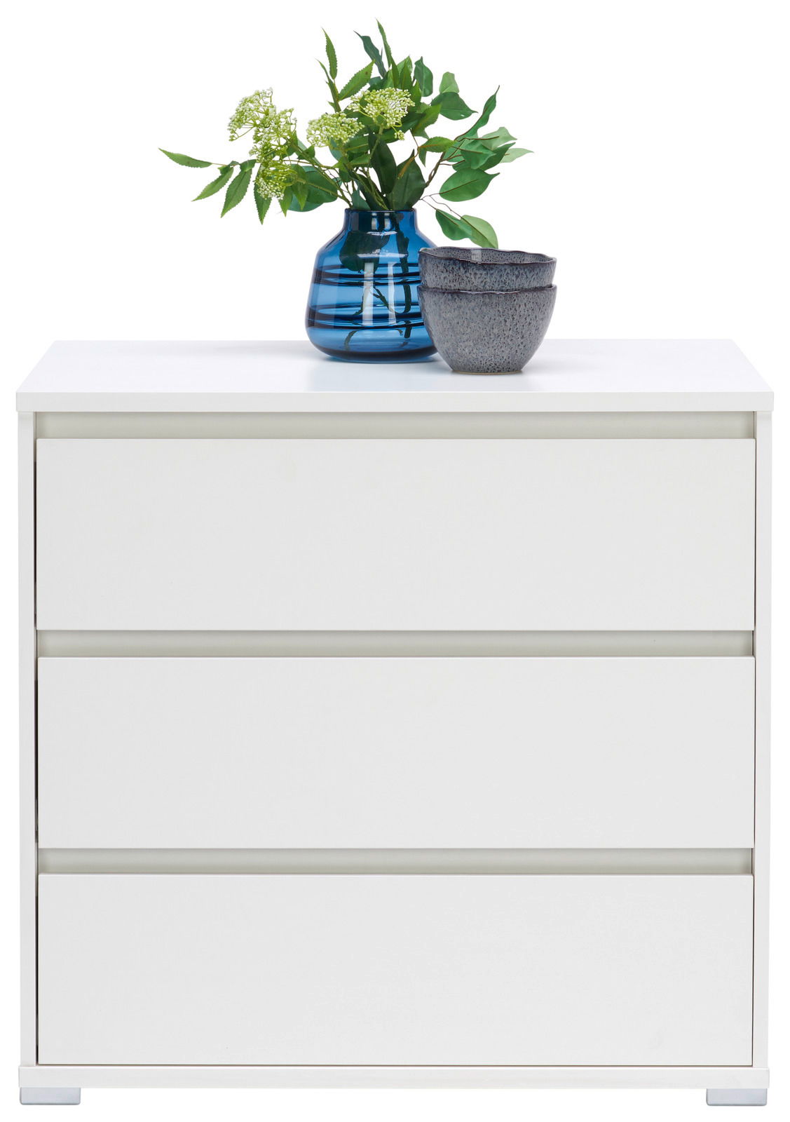 Weiße Kommode mit drei Schubladen, darauf eine blaue Vase mit grünen Pflanzen und zwei graue Schalen, frontale Perspektive.