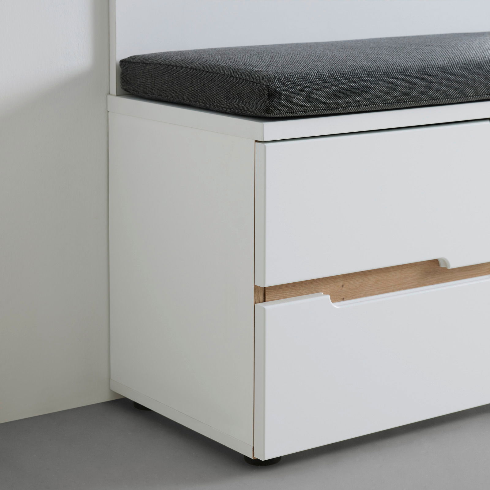 Weiße Bank mit grauem Sitzkissen, seitliche Perspektive, zeigt Schubladen mit Holzdetails.