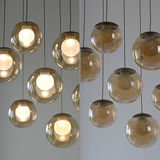 Moderne LED-Pendelleuchte mit mehreren kugelförmigen, transparenten Lampenschirmen, von unten betrachtet.