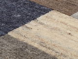 Nahaufnahme eines Wollteppichs mit einem geometrischen Muster in verschiedenen Brauntönen und Beige, von oben betrachtet.
