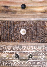 Nahaufnahme von Schubladenfronten mit verschiedenen Holzstrukturen und dekorativen Griffen, von oben nach unten: schwarze, weiße und bronzefarbene Griffe.