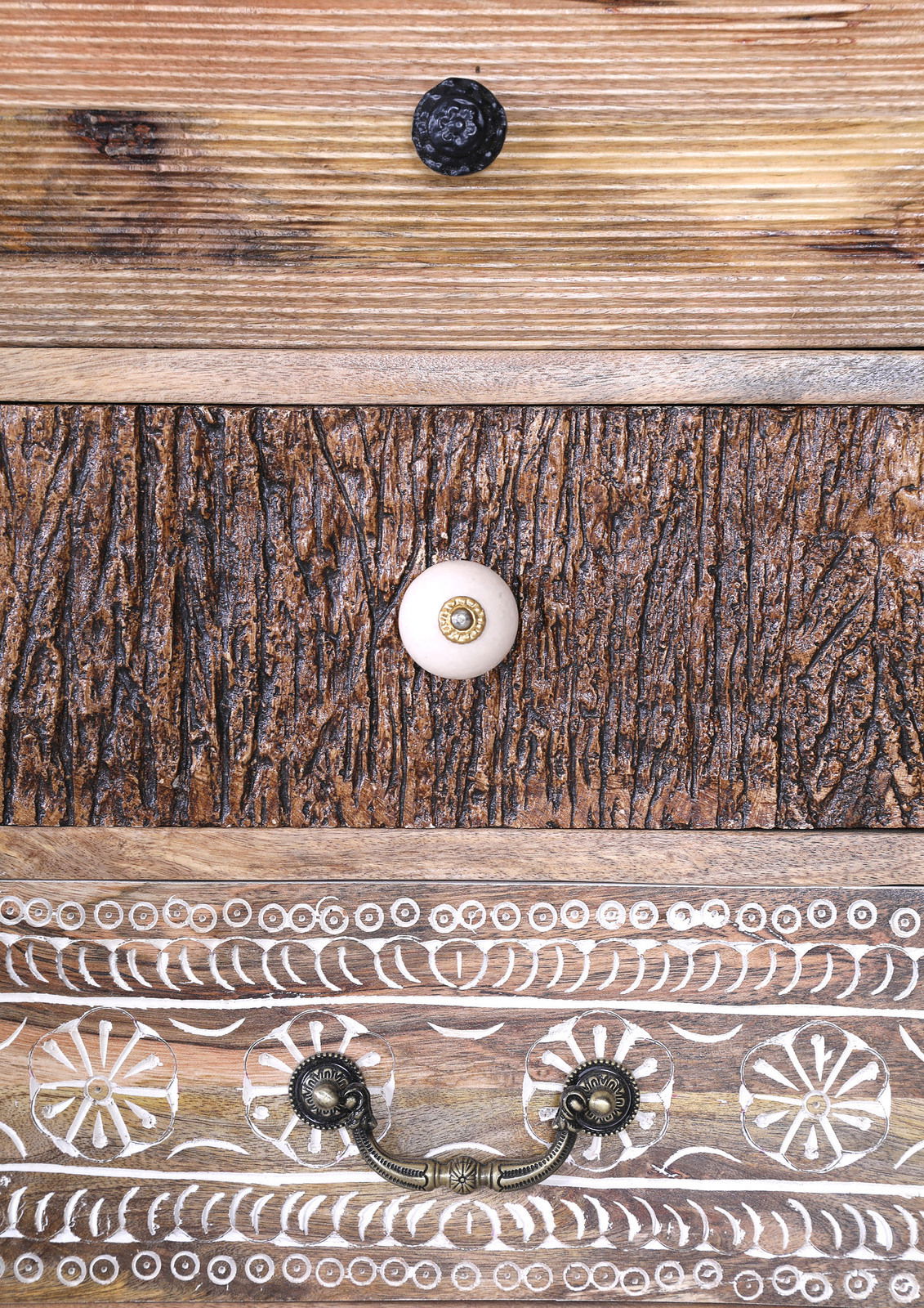 Nahaufnahme von Schubladenfronten mit verschiedenen Holzstrukturen und dekorativen Griffen, von oben nach unten: schwarze, weiße und bronzefarbene Griffe.