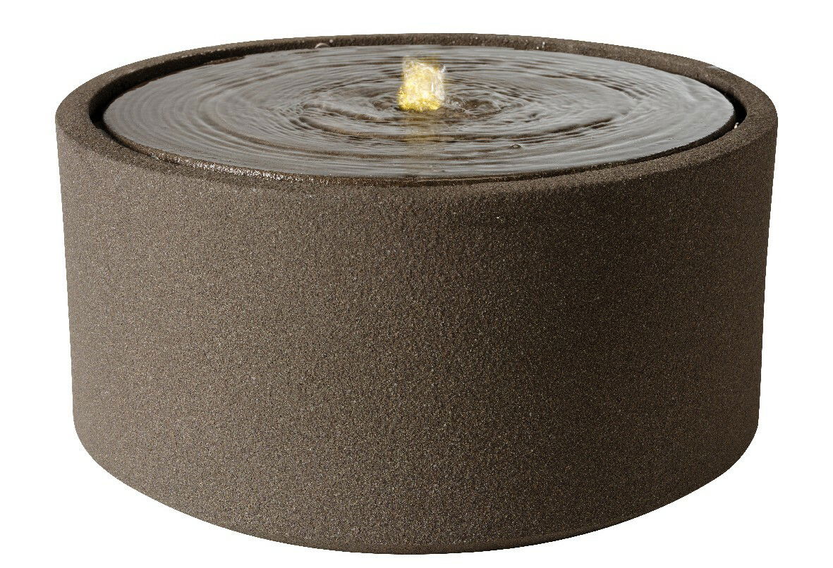 Runder, moderner Brunnen aus dunklem Material mit sprudelndem Wasser an der Oberseite, seitliche Perspektive