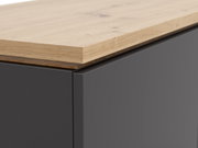 Nahaufnahme eines Highboards mit einer Kombination aus einer glatten, dunklen Oberfläche und einer natürlichen Holzplatte, perspektivisch von der Seite aufgenommen.