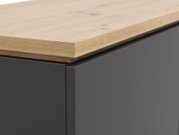 Nahaufnahme eines Highboards mit einer Kombination aus einer glatten, dunklen Oberfläche und einer natürlichen Holzplatte, perspektivisch von der Seite aufgenommen.