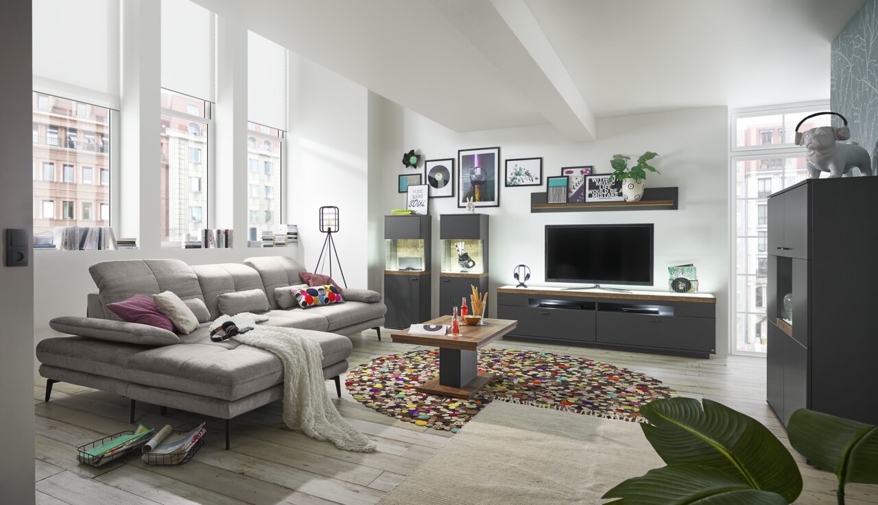 Moderne Wohnzimmeransicht mit einer großen, grauen Rundecke im Vordergrund, umgeben von stilvollen Möbeln und Dekorationen in einem hellen Raum.