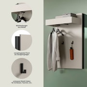 Moderne Wandgarderobe in Weiß mit vorspringender Ablage, Metall-Kleiderstangen und schwarzen Haken; schräg von vorn (3/4-Perspektive) an der Wand montiert, mit Bügeln und hängendem Bademantel