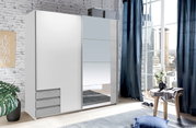Moderner, zweiflügeliger Schwebetürenschrank in Weiß mit Spiegel, seitliche Perspektive, in einem hellen Raum mit großen Fenstern und urbanem Ausblick.