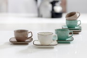 Drei Espressotassen mit Untertassen in verschiedenen Farben (grau, weiß, grün) auf einem Tisch, aus seitlicher Perspektive fotografiert.