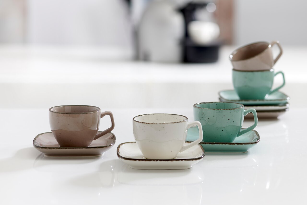 Ritzenhoff & Breker Espressokopje CASA Drei Espressotassen mit Untertassen in verschiedenen Farben (grau, weiß, grün) auf einem Tisch, aus seitlicher Perspektive fotografiert.