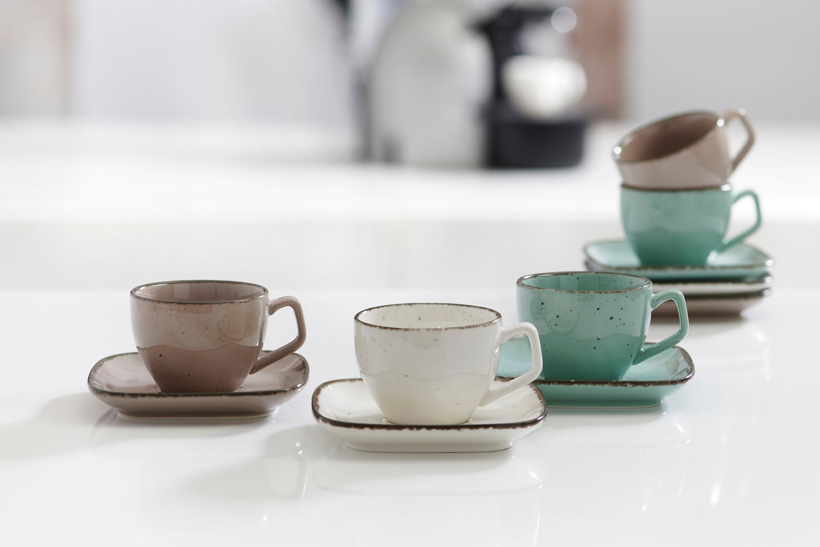 Drei Espressotassen mit Untertassen in verschiedenen Farben (grau, weiß, grün) auf einem Tisch, aus seitlicher Perspektive fotografiert.