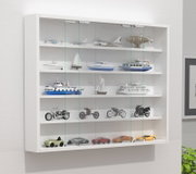 Wandmontierte weiße Sammlervitrine mit Glas-Schiebetüren und mehreren Regalböden, bestückt mit Modellfahrzeugen (Flugzeuge, Schiffe, Motorräder, Autos), schräg von vorne links fotografiert.
