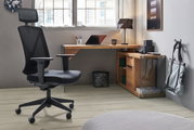 Moderner Eck-Schreibtisch aus Holz in einem stilvollen Büro, mit einem ergonomischen Bürostuhl im Vordergrund. Perspektive von der Seite.