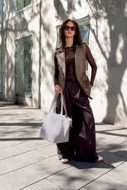 Graue Stoff-Tragetasche mit langen Henkeln, von einer Frau im Streetstyle-Outfit getragen, Outdoor vor modernem Gebäude; Perspektive: frontale Ganzkörperaufnahme auf Augenhöhe.