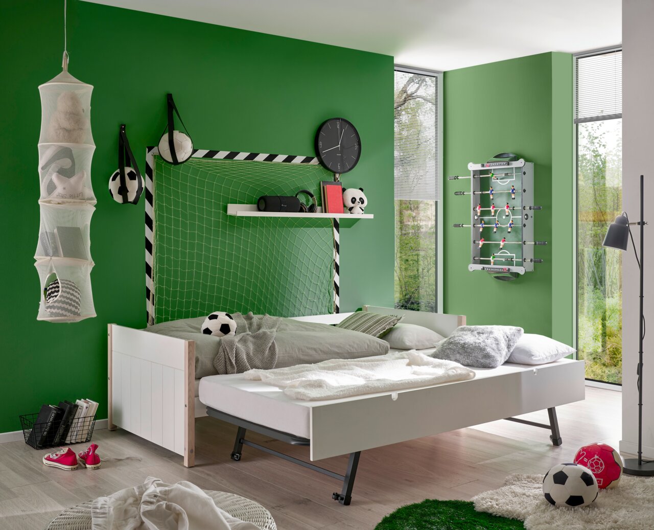 Jugendbett in einem Fußball-Themenzimmer mit grüner Wand, Fußball-Dekorationen und Tischkicker an der Wand, seitliche Perspektive