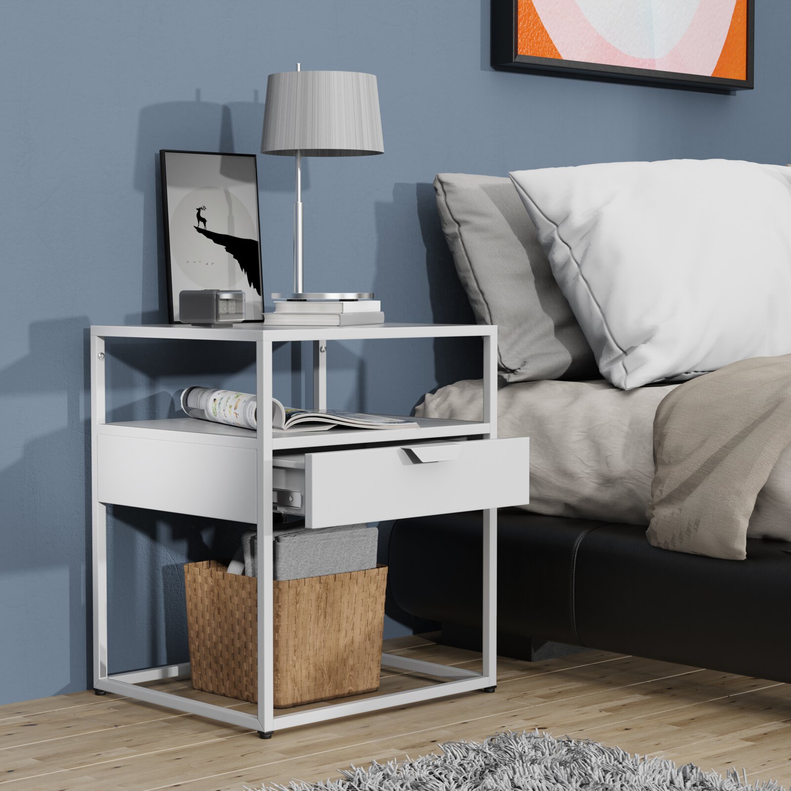 Weißer moderner Nachttisch mit Metallrahmen und halb geöffneter Schublade neben einem Bett, darauf Lampe und Deko Ansicht schräg von vorn.