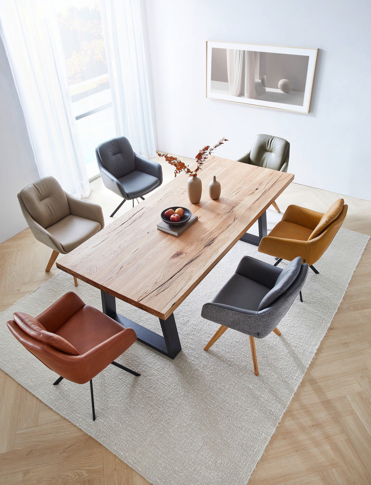 Esszimmer mit einem großen Holztisch und sechs verschiedenen Armlehnstühlen in einer modernen, hellen Umgebung, aus der Vogelperspektive betrachtet.