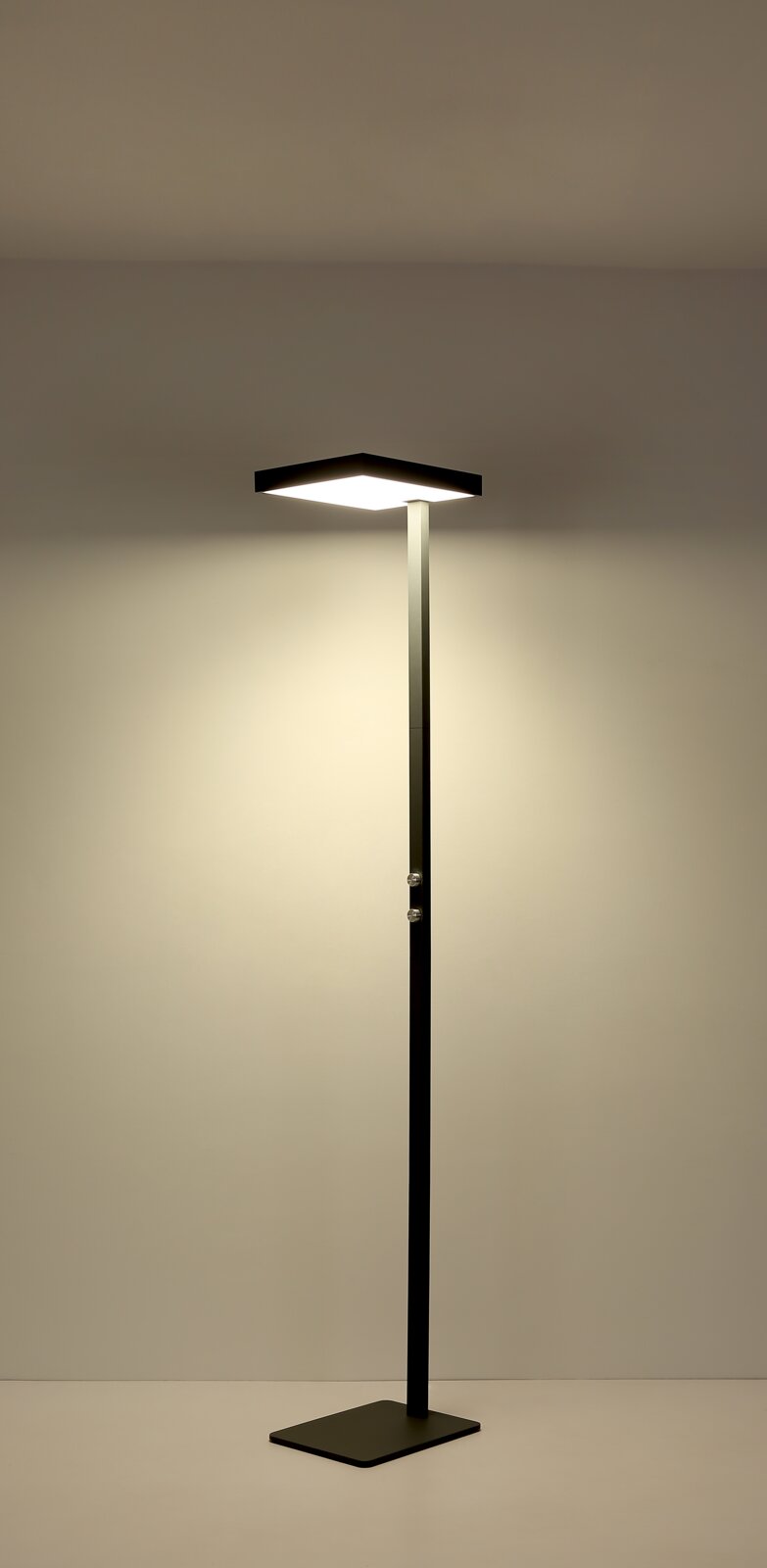 Schlanke schwarze LED-Stehleuchte mit quadratischem Leuchtkopf und rechteckigem Standfuß, eingeschaltet, frontale Ansicht auf neutralem Hintergrund