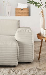 Nahaufnahme einer modernen, cremefarbenen Rundecke mit geripptem Stoffbezug, von der Seite betrachtet. Im Hintergrund sind eine Holzzeitschriftenhalterung, eine dekorative Vase und ein Beistelltisch zu sehen.