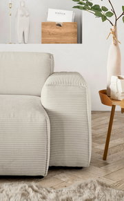 Nahaufnahme einer modernen, cremefarbenen Rundecke mit geripptem Stoffbezug, von der Seite betrachtet. Im Hintergrund sind eine Holzzeitschriftenhalterung, eine dekorative Vase und ein Beistelltisch zu sehen.