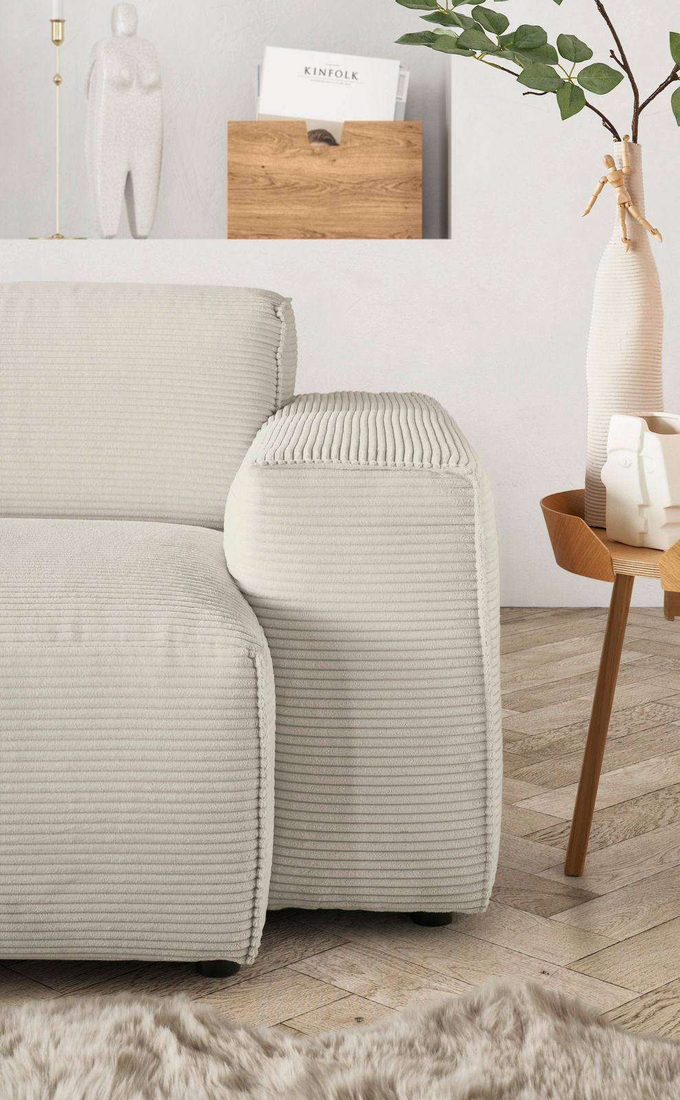 Nahaufnahme einer modernen, cremefarbenen Rundecke mit geripptem Stoffbezug, von der Seite betrachtet. Im Hintergrund sind eine Holzzeitschriftenhalterung, eine dekorative Vase und ein Beistelltisch zu sehen.