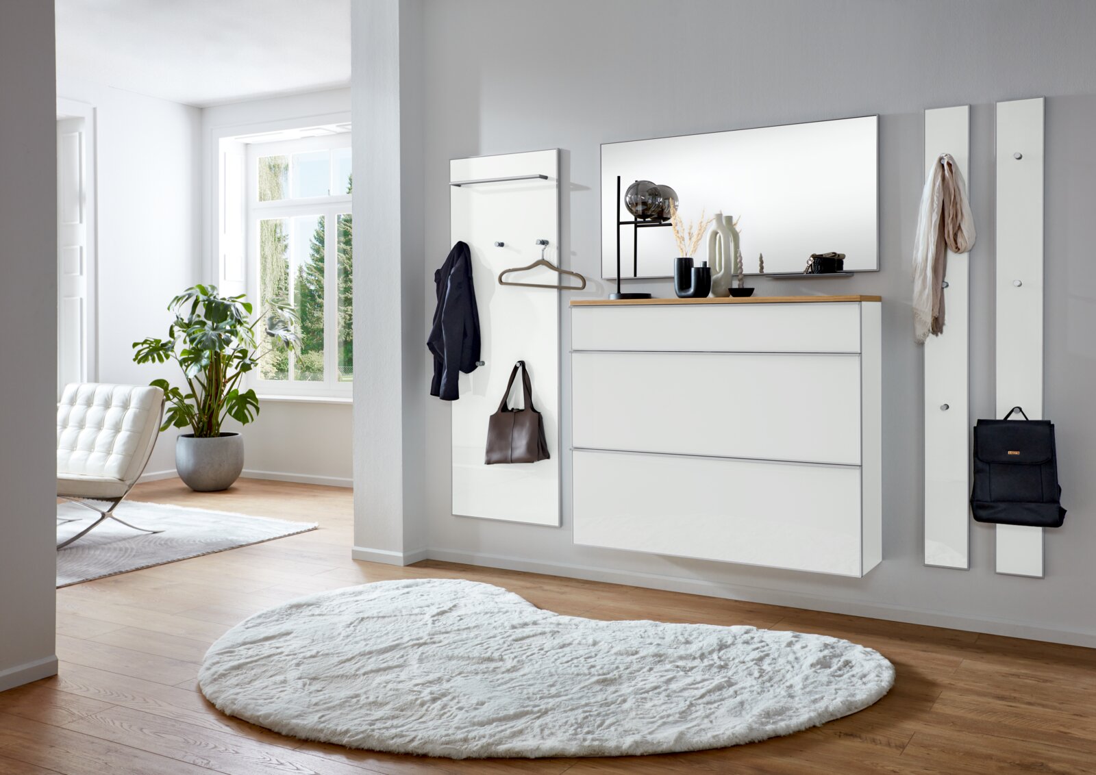 Modernes weißes Garderoben-Set im Flur mit Wandpaneel, Haken, Spiegel und schwebender Kommode mit Holzablage, seitliche Perspektive im hellen Raum
