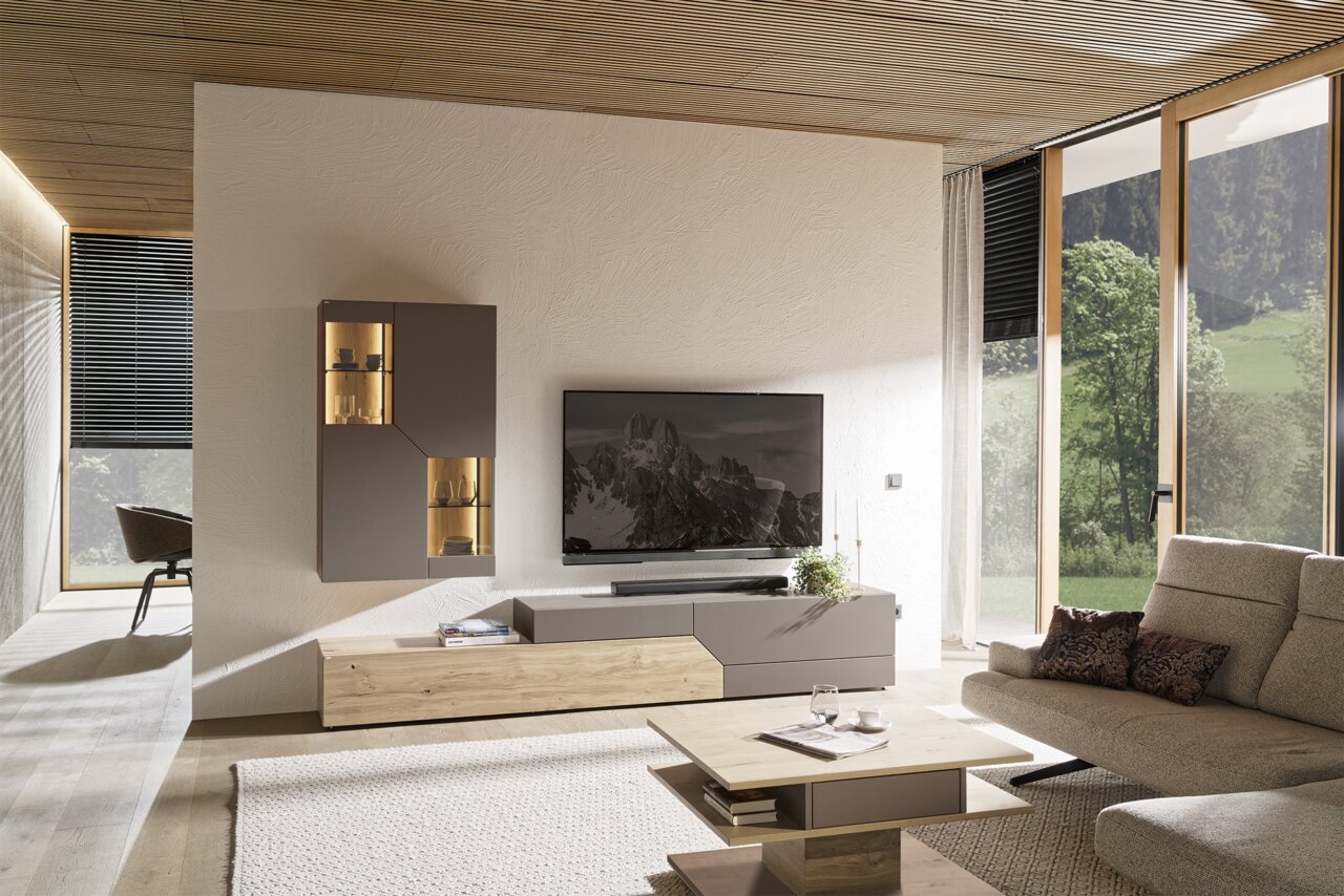 Moderne woonkamer met tv-wandmeubel in grijs en houtlook, hangende vitrinekast met verlichting en lowboard onder een flatscreen-tv; perspectief: frontaal, licht zijdelings groothoekbeeld.
