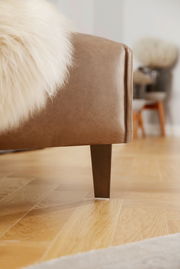 Nahaufnahme einer braunen Polsterrundecke mit Holzbein, seitliche Perspektive