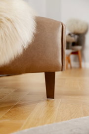 Nahaufnahme einer braunen Polsterrundecke mit Holzbein, seitliche Perspektive