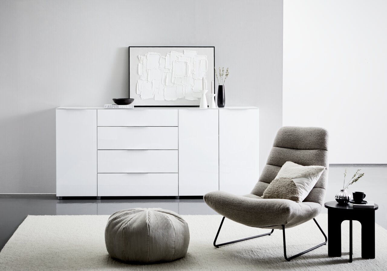 Modernes weißes XL-Sideboard mit Hochglanzoberfläche, frontal abgebildet in einem stilvollen Wohnzimmer mit dekorativen Elementen.