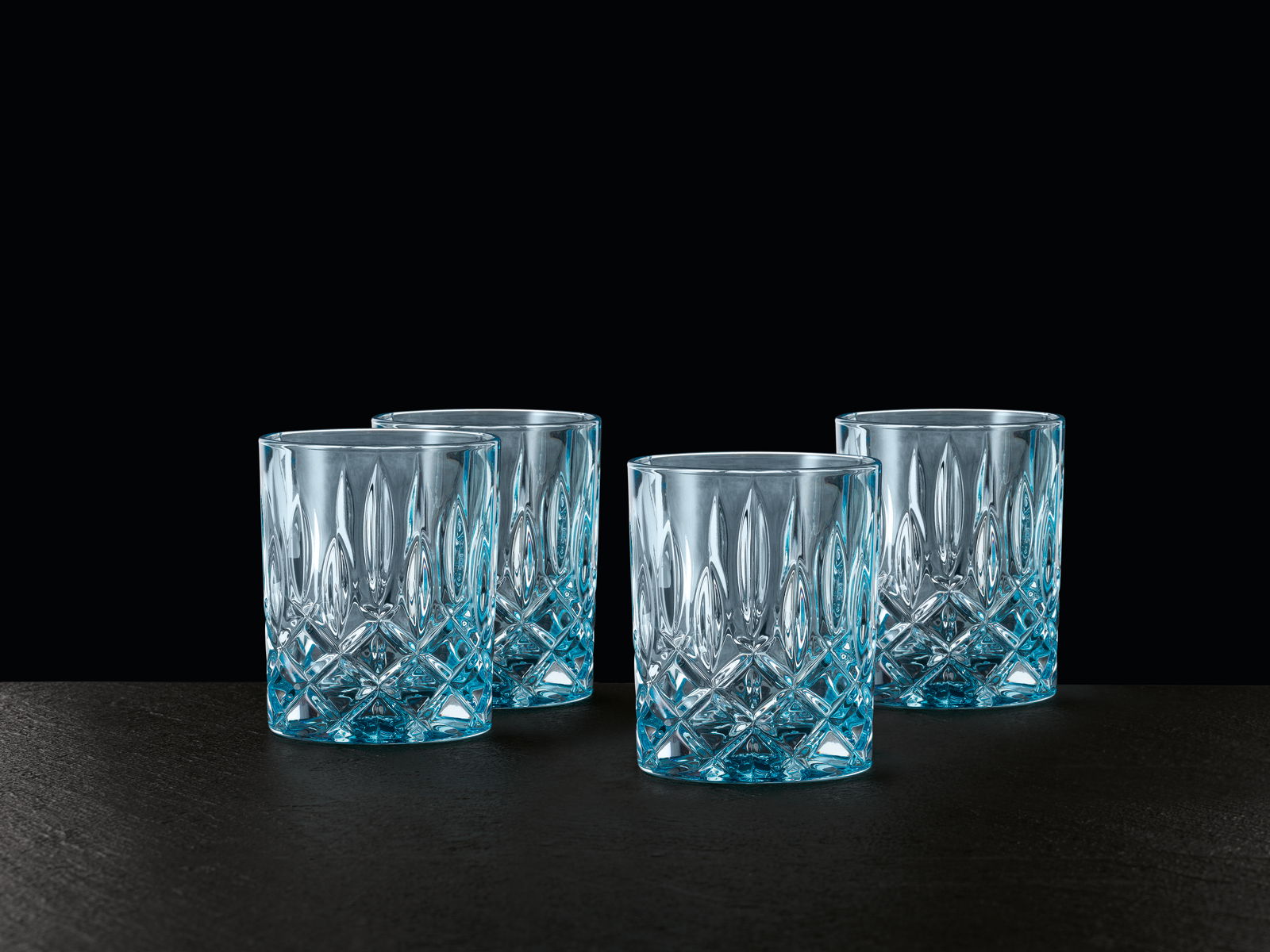 Vier elegante Whiskybecher aus Kristallglas mit facettiertem Design, seitliche Perspektive.