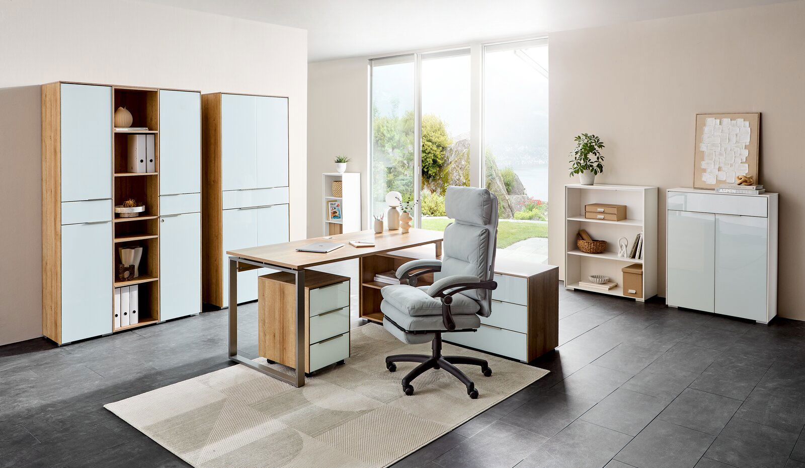 Moderne Büroumgebung mit Eckschreibtisch NEVADA, Aktenschränken und Rollcontainer in heller Holzoptik und weißen Fronten, seitliche Perspektive.